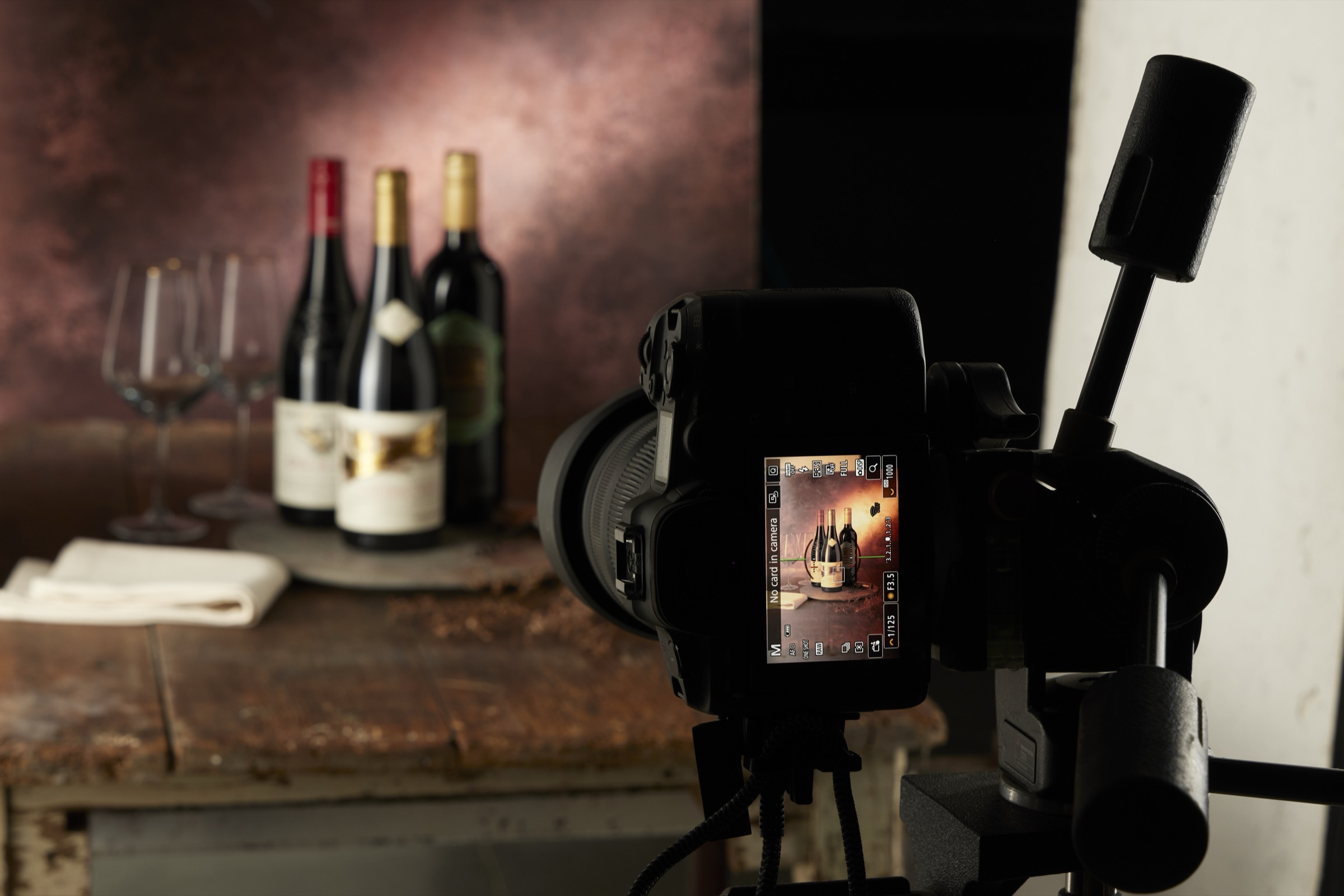 A drinks shoot in progress on the studio floor: wine bottles on a rustic tabletop against a painted backdrop